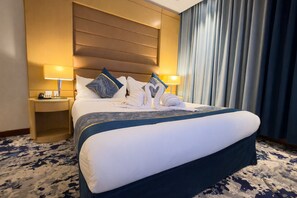 Een hotelkamer met een groot bed, twee nachtkastjes met lampen, een hoofdbord en een raam met gordijnen.