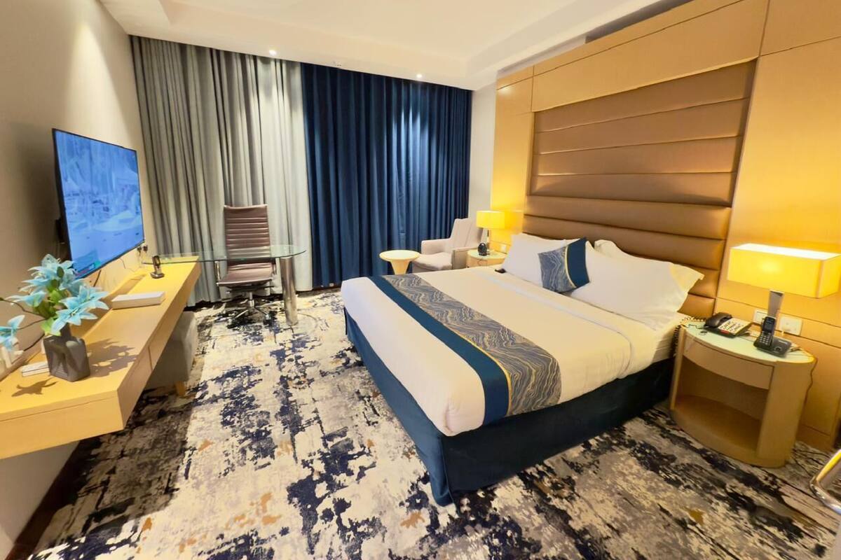 Une chambre d’hôtel avec un grand lit, un bureau avec une télévision, une chaise, une lampe et une table de chevet.