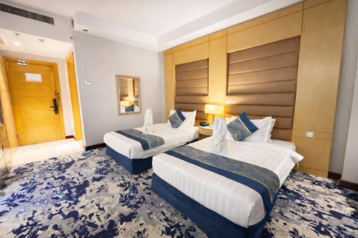 Une chambre d’hôtel avec deux lits, une tête de lit en bois, un grand miroir et une moquette à motifs.