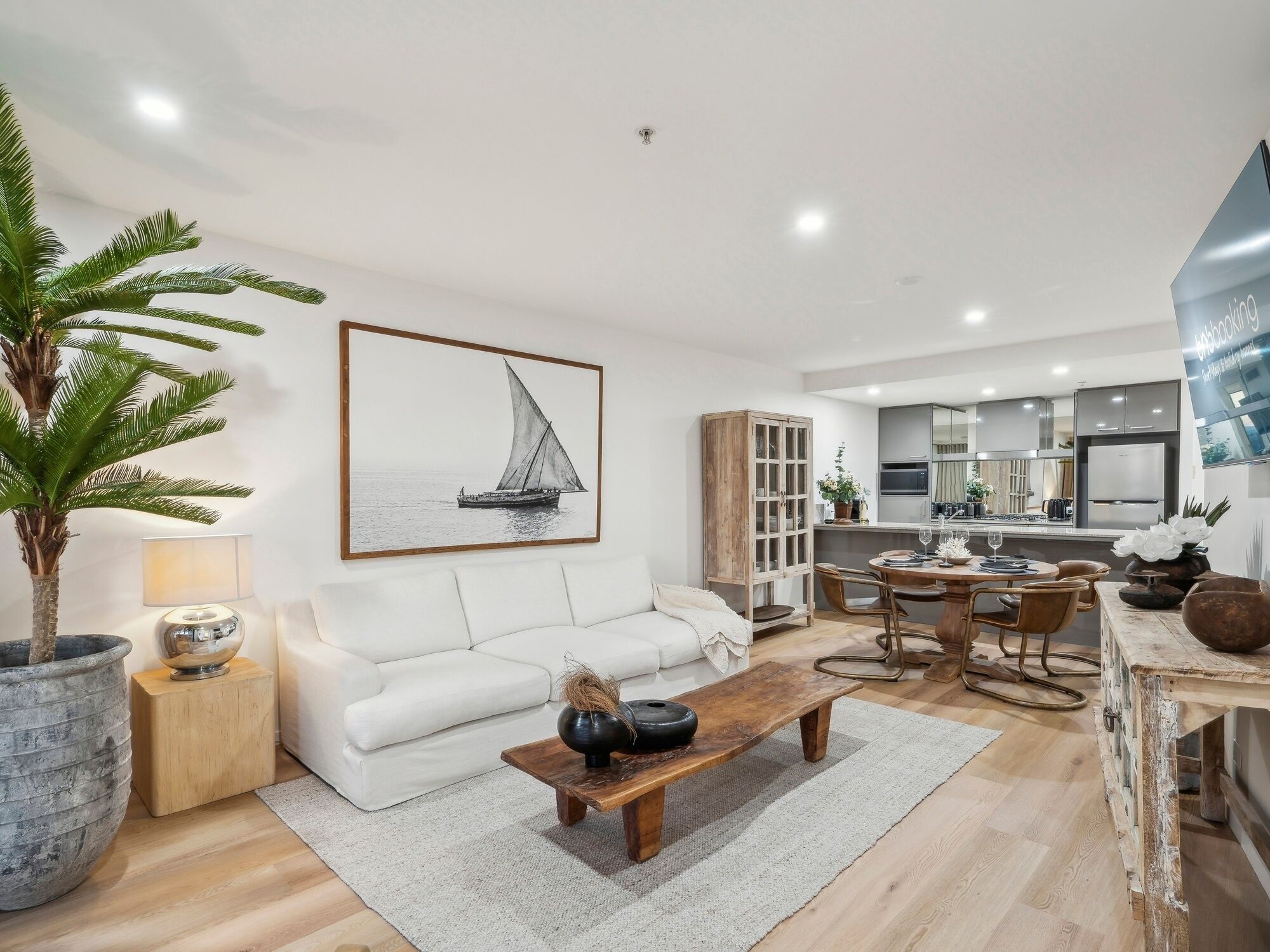 A modern living room with a white sofa, a wooden coffee table, and a large potted plant.