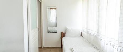 Un dormitorio con cama, espejo y ventana con cortinas.