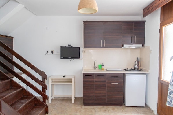 Une cuisine compacte avec des meubles de couleur bois foncé, un plan de travail blanc, un petit réfrigérateur blanc et un escalier en bois.