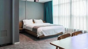 A hotel room with a bed, a table, and a window with curtains. - Huile Holiday Hostel (Shanghai)
