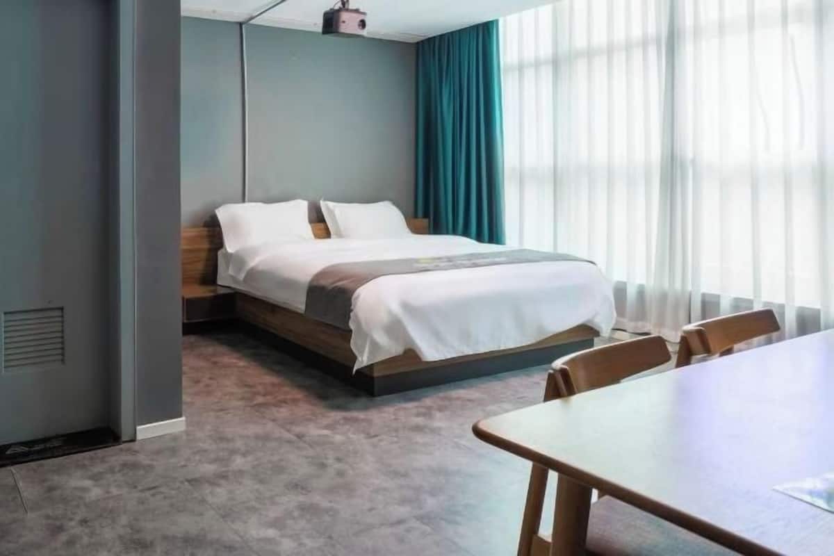 A hotel room with a bed, a table, and a window with curtains.