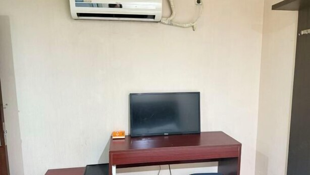 A room with a wooden desk, a television, a small trash bin, and an air conditioning unit mounted on the wall. - Huile Holiday Hostel (Shanghai)