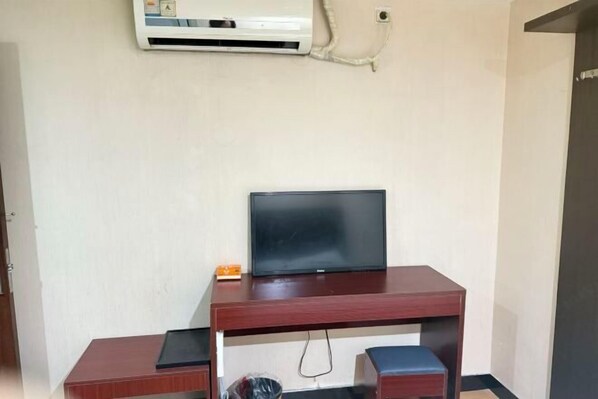 A room with a wooden desk, a television, a small trash bin, and an air conditioning unit mounted on the wall. - Huile Holiday Hostel (Shanghai)