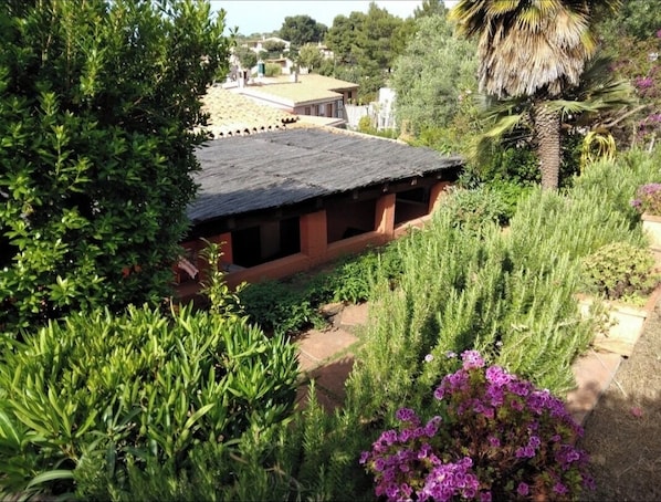 A rustic building with a sloped roof surrounded by lush greenery and flowering plants.