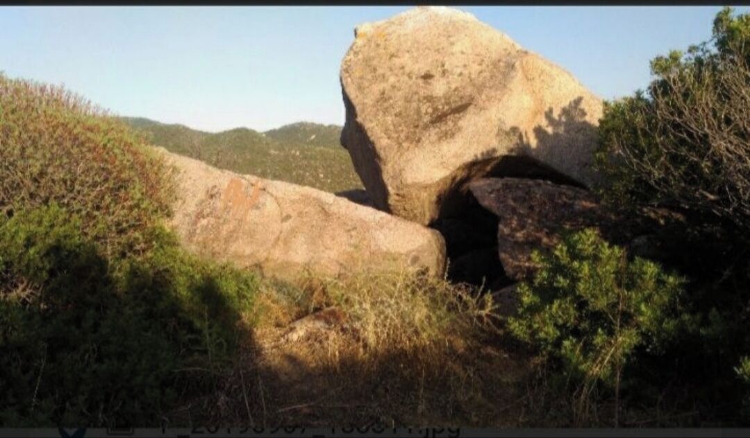 Une grande formation rocheuse dotée d’une arche naturelle, le tout étant entouré de végétation.