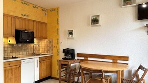 Una cocina compacta con armarios de madera, un microondas, una cafetera y una mesa de comedor con sillas.