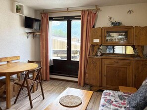 Una habitación acogedora con una mesa de madera, sillas, un tapete tejido, un sofá y un armario con puertas de cristal.