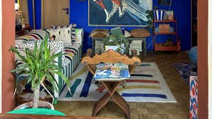 Ein lebhaftes Wohnzimmer mit blauer Wand, einem großen abstrakten Gemälde, einem Holztisch und verschiedenen farbenfrohen Kissen.