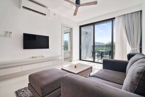 Un salon moderne doté d’un téléviseur à écran plat, de canapés gris, d’une table basse et d’un balcon avec une table et des chaises.
