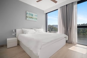 Une chambre moderne avec un grand lit, une table de chevet, un tableau au mur et une vue sur l’extérieur grâce à une grande fenêtre.