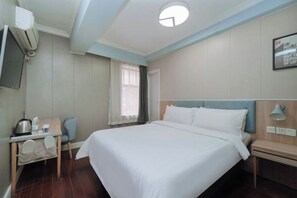 A hotel room with a bed, a desk with a kettle, a chair, a TV, and a bedside table with a lamp. - Pebble Motel (Shanghai Jinqiao Metro YanggaoRoad) (Shanghai)