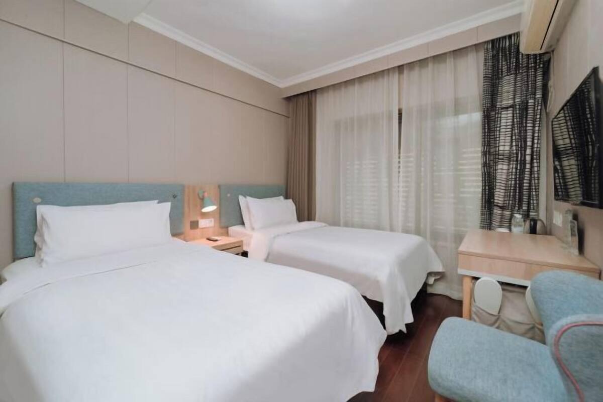 Ett hotellrum med två sängar, ett skrivbord, en stol, en tv och ett fönster med gardiner.