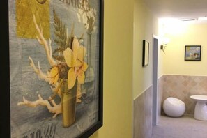 A framed artwork of flowers in a vase on a wall, a white toilet, and a wall-mounted light fixture in a bathroom. - Pebble Motel (Shanghai Jinqiao Metro YanggaoRoad) (Shanghai)