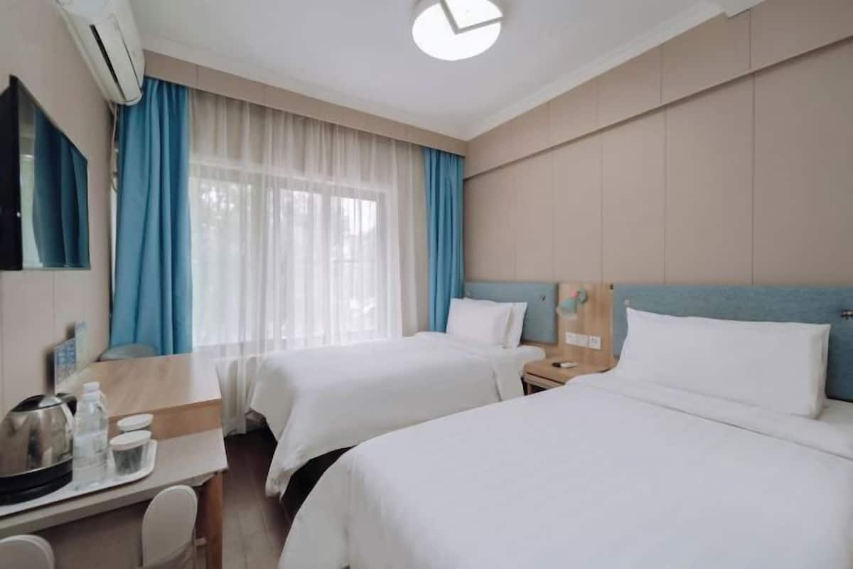 Ett hotellrum med två sängar, ett skrivbord med en vattenkokare, en spegel och ett fönster med gardiner.