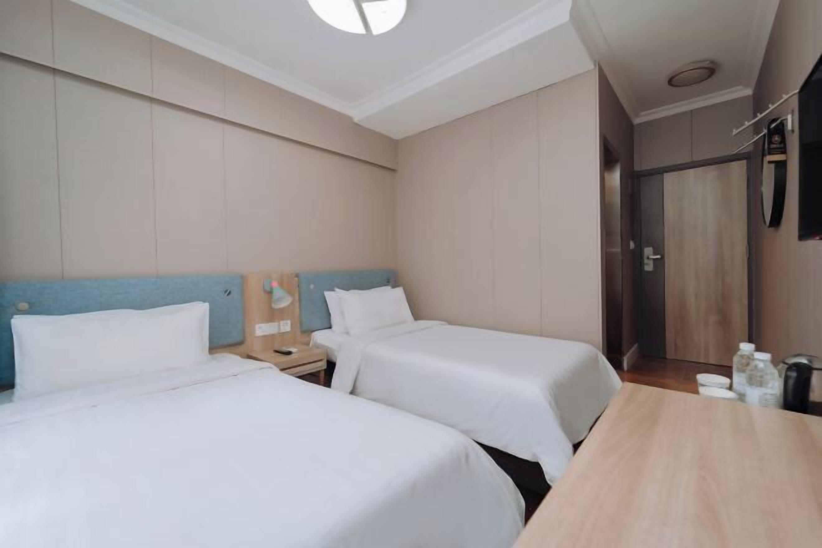 A hotel room with two beds, a wooden table, a nightstand, and a mirror on the wall.