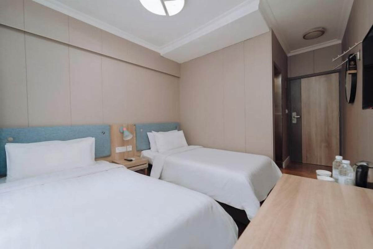 Quarto de hotel com duas camas, uma mesa de madeira, um criado-mudo e um espelho na parede.