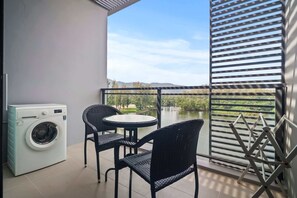 Un balcon équipé d’un lave-linge, de deux chaises, d’une table et offrant une vue sur un lac et des montagnes.