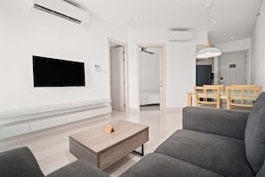 Una sala de estar moderna con un televisor de pantalla plana montado en la pared, una mesa de centro de madera y sofás grises.