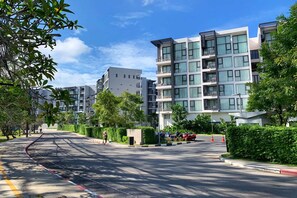 A modern multi-story residential building with balconies, a clear sky, and a road with traffic cones.