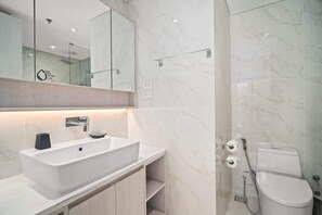 Un baño moderno con un lavamanos grande de color blanco, un espejo encima y un inodoro con ducha.