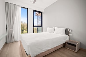 Une chambre à coucher moderne avec un grand lit, une table de chevet et une vue sur l’extérieur par une fenêtre.