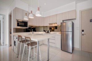 Une cuisine moderne dotée d’un îlot central, d’appareils électroménagers en acier inoxydable et de luminaires suspendus.