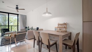 A modern living room with a dining area, large windows, ceiling fan, and a wooden table with chairs. - Cassia Residences, Two-Bedroom 2610 D Premium (Choeng Thale)