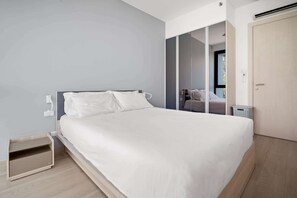 A modern bedroom with a bed, a small wooden nightstand, a wardrobe, and a sliding door leading to a bathroom.