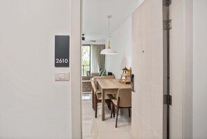 A modern dining area with a wooden table and chairs, a pendant light, and a view of a balcony with curtains.