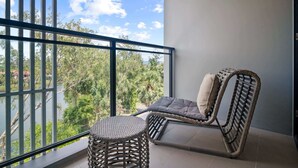 A balcony with a wicker chair and a round stool, overlooking a body of water and greenery. - Cassia Residences, Two-Bedroom 2610 D Premium (Choeng Thale)