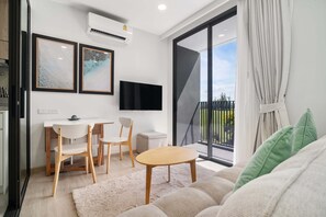 A modern living room with a sofa, a small table, a TV, and a balcony with a view.