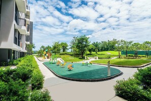 Un terrain de jeux avec des balançoires et des toboggans, entouré de verdure et bordé d’un bâtiment doté de balcons.