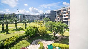 A residential building complex with multiple balconies, a landscaped garden with palm trees, and a clear sky.