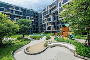 A modern apartment complex with a playground, green spaces, and a curved pathway.