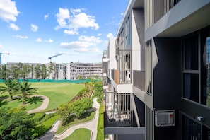 Um edifício moderno com varandas, vista para um parque verde e guindastes de construção ao fundo.