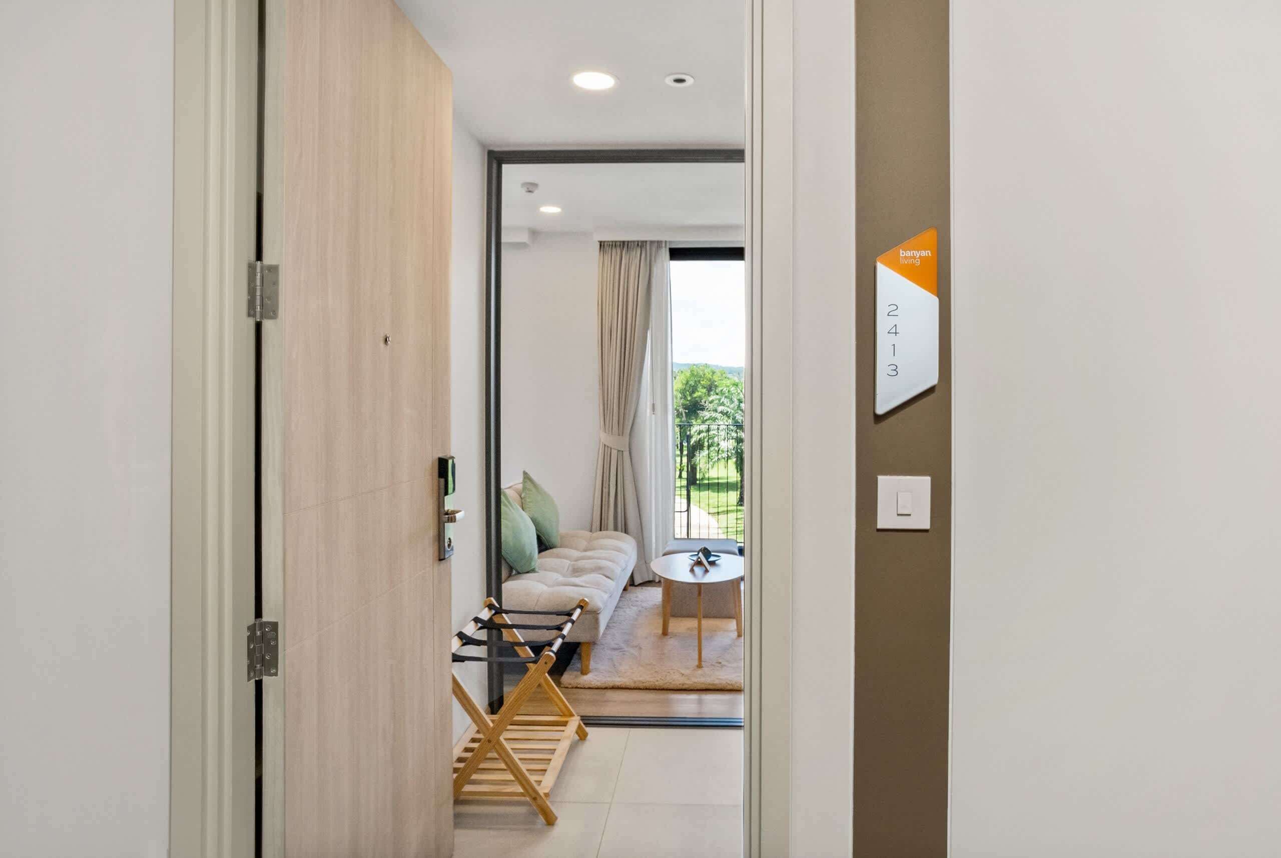 A hotel room with a wooden door, a view of a balcony, a sofa, a small round table, and a sign indicating room number 2413.