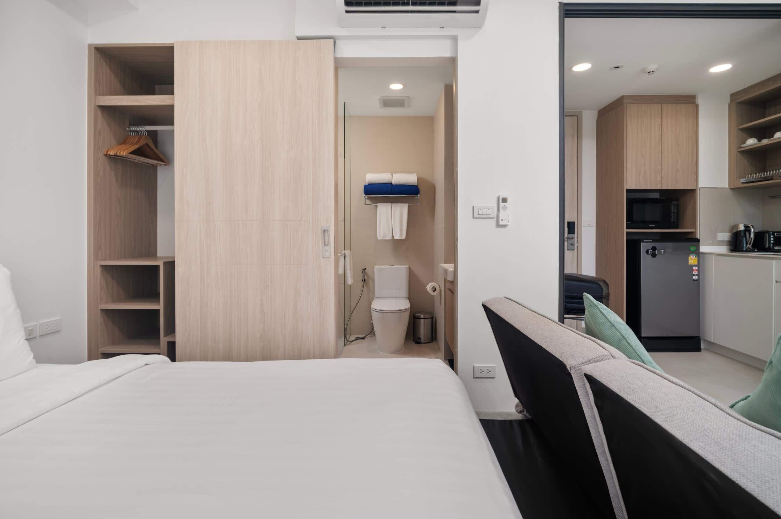 Hotellihuone, jossa on sänky, vaatekaappi, kylpyhuone ja pieni keittiönurkkaus.