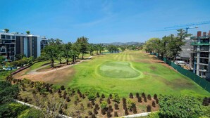 Un campo de golf con un green impecable, rodeado de árboles y edificios modernos.