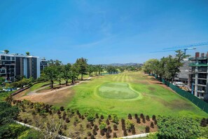 A golf course with a well-maintained green, surrounded by trees and modern buildings.