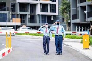 Dos personas con uniforme de pie en una entrada con puerta y un edificio moderno al fondo.