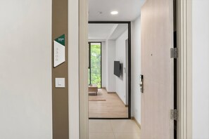 Un pasillo con una puerta a la derecha, un interruptor de luz y una placa numerada en la pared.