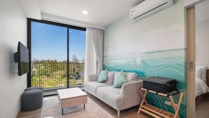 Une chambre d’hôtel moderne dotée d’un grand balcon, d’un canapé avec des coussins, d’une petite table, d’un lit et d’un téléviseur fixé au mur.