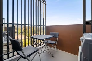 A balcony with a table and two chairs, a grill, and a view of trees and buildings. - Skypark Aurora 2, Two-Bedroom 2Cx1 Premium (Choeng Thale)