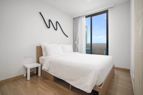 A modern bedroom with a wooden bed, white bedding, a small bedside table, and a large window with curtains.