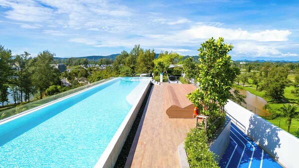 A long swimming pool with a wooden deck and a view of a river and greenery. - Skypark Aurora, One Bedroom 3709 1Bx Premium (Choeng Thale)
