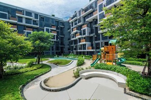 A modern apartment complex with a playground, green spaces, and a curved pathway.