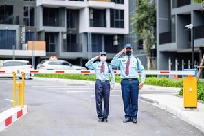 Two uniformed individuals standing at a gated entrance with a modern building in the background. - Skypark Aurora, One Bedroom 3709 1Bx Premium (Choeng Thale)